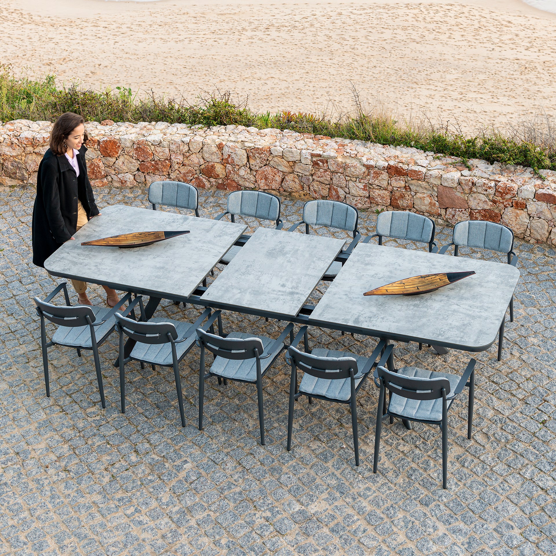 Outdoor Rimini dining table with a tempered glass top being extended by a woman pressing the mechanism and opening the table