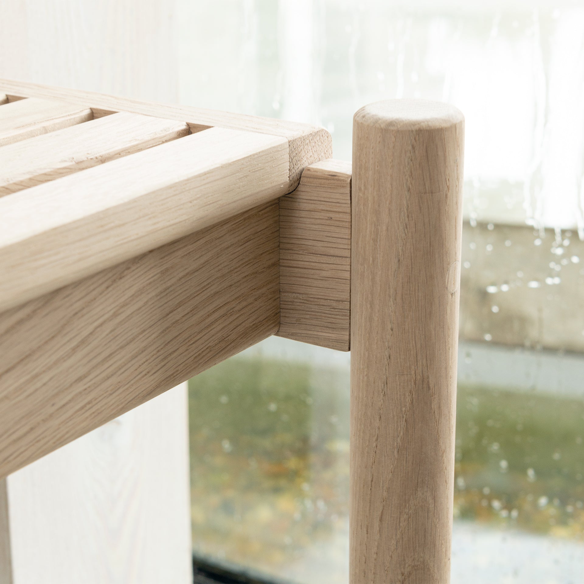 Close-up of the detail of Trak indoor European light oak bench with modern rounded tubular legs