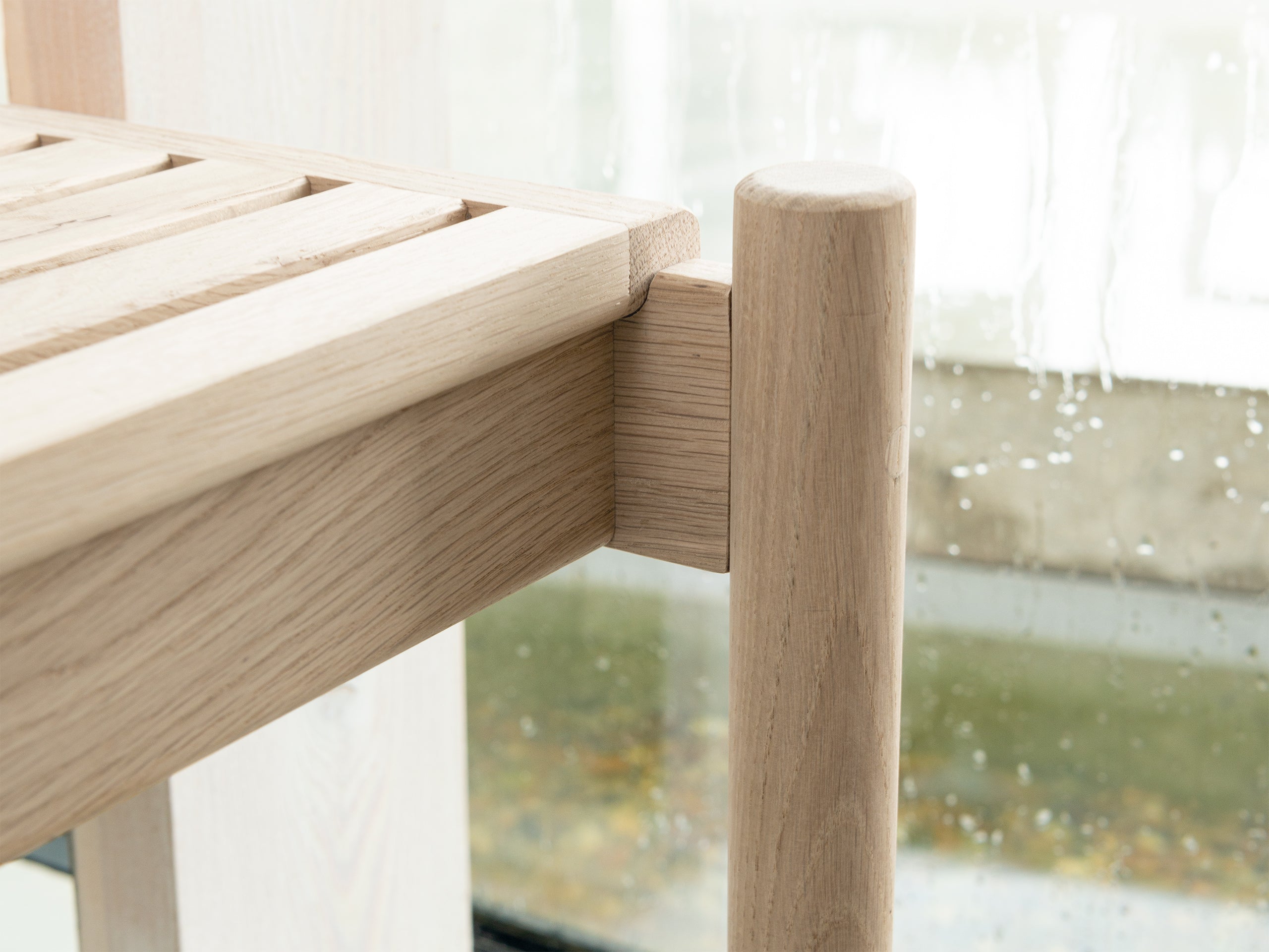 Close-up of the detail of Trak indoor European light oak bench with modern rounded tubular legs
