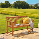 Wooden bench with a yellow cushion and a tray of items on a patio with a scenic background