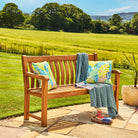 Wooden bench with colorful pillows and a blanket in a garden setting