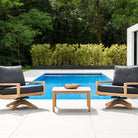Two tivoli swivel loung chairs with black cushions  and a square wooden coffee table by a pool 