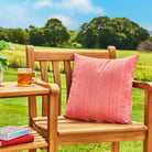 Wooden chair with a pink cushion and a glass of tea on a table outdoors.