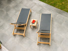 Two wooden lounge chairs with dark cushions on a tiled patio, accompanied by a small table with watermelon.