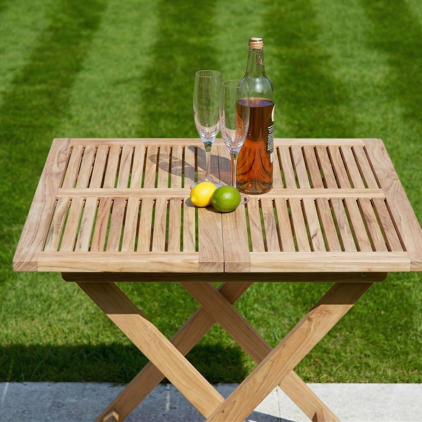 Wooden table with a bottle, glasses, and fruits on a grassy background