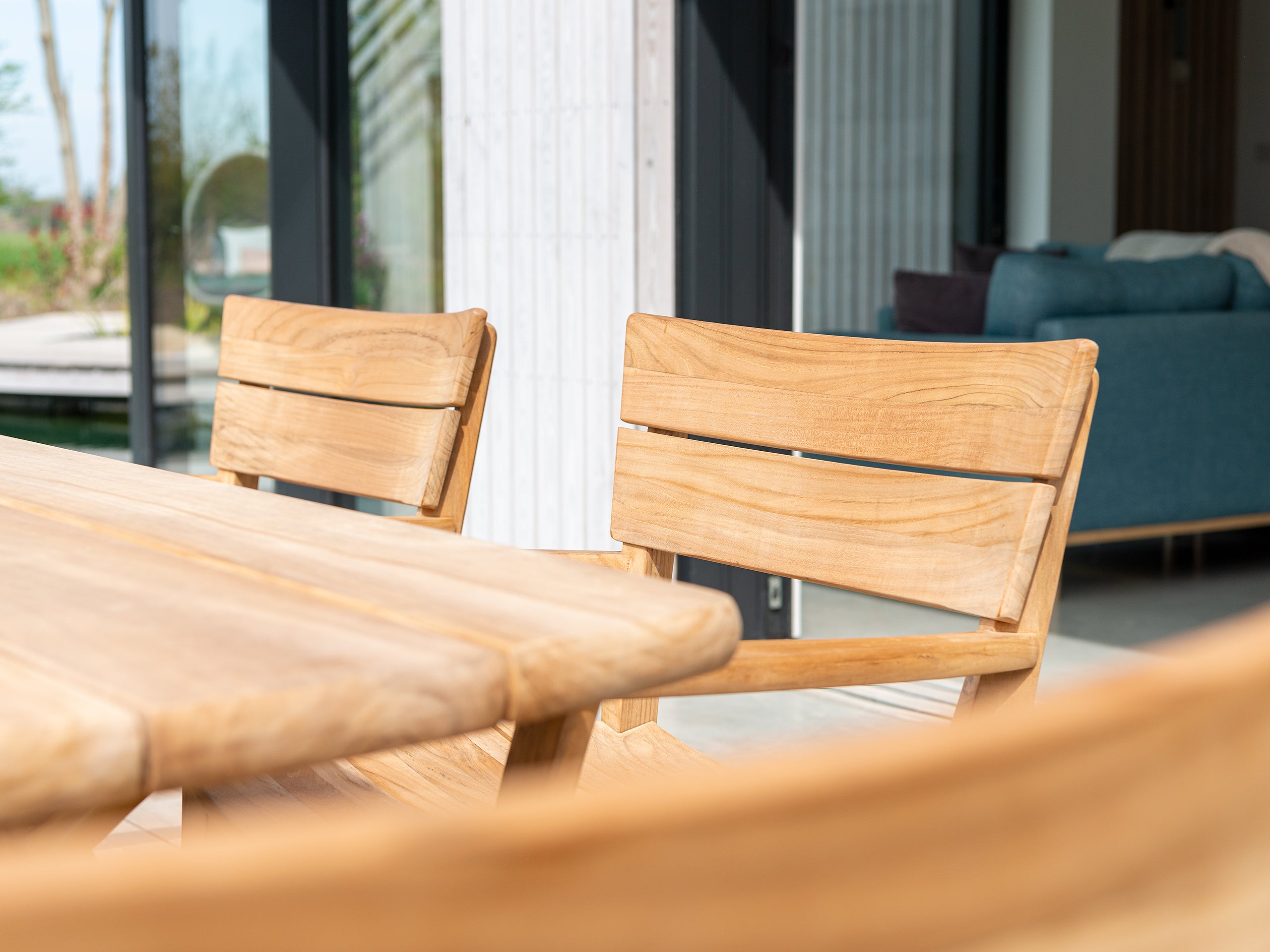 Wooden outdoor table and chairs with a blurred background of a modern house.