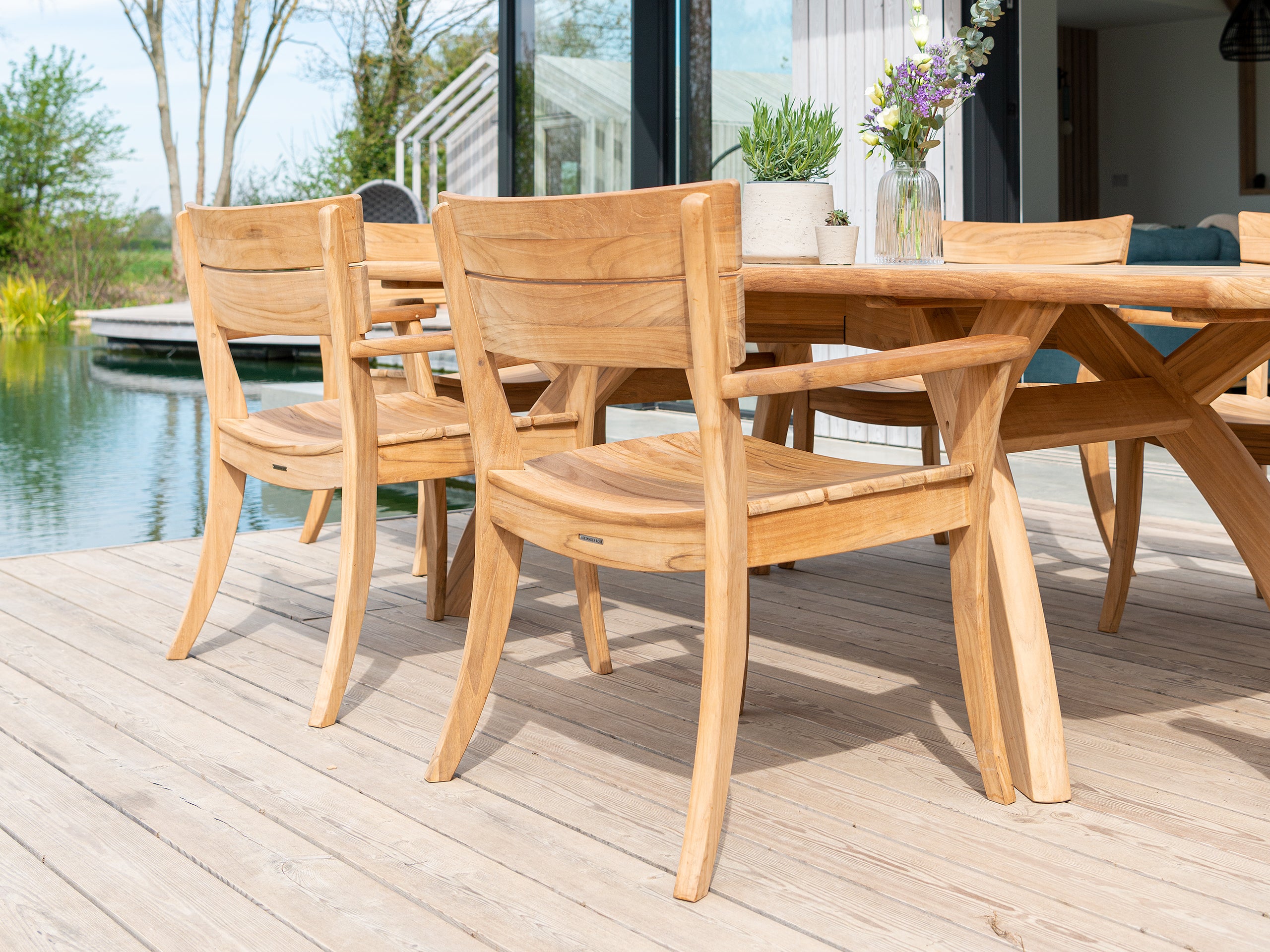 Wooden outdoor dining table and chairs on a deck with a pool in the background