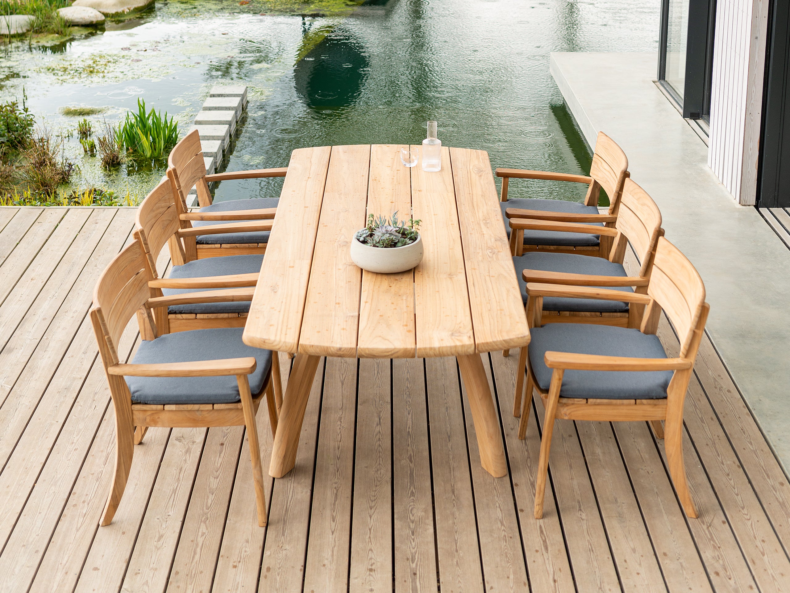 Wooden outdoor dining table with chairs on a deck by a body of water. This to illustrate the chair seat cushion.