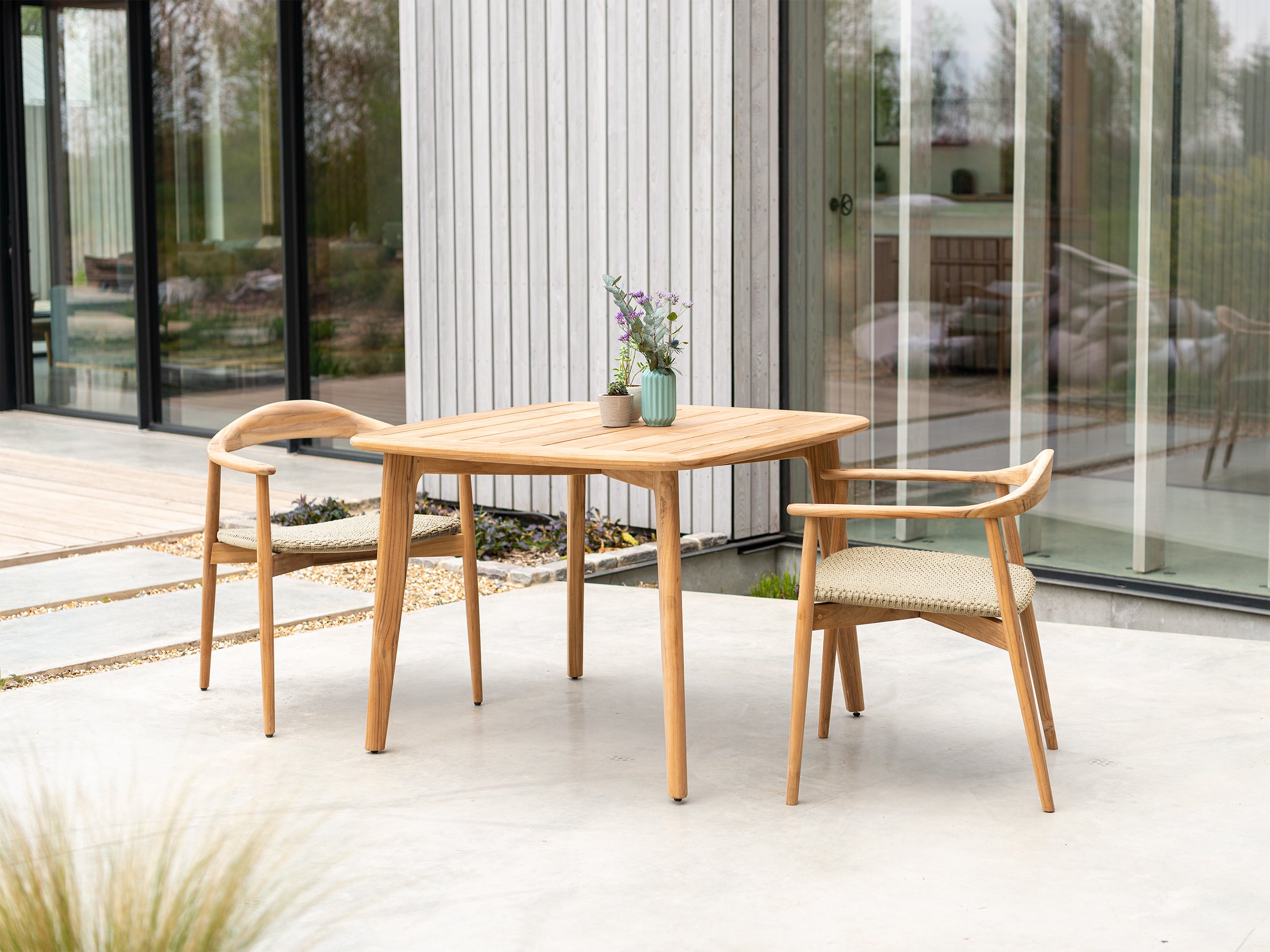 Square teak outdoor dining table and two curved dining armchairs
