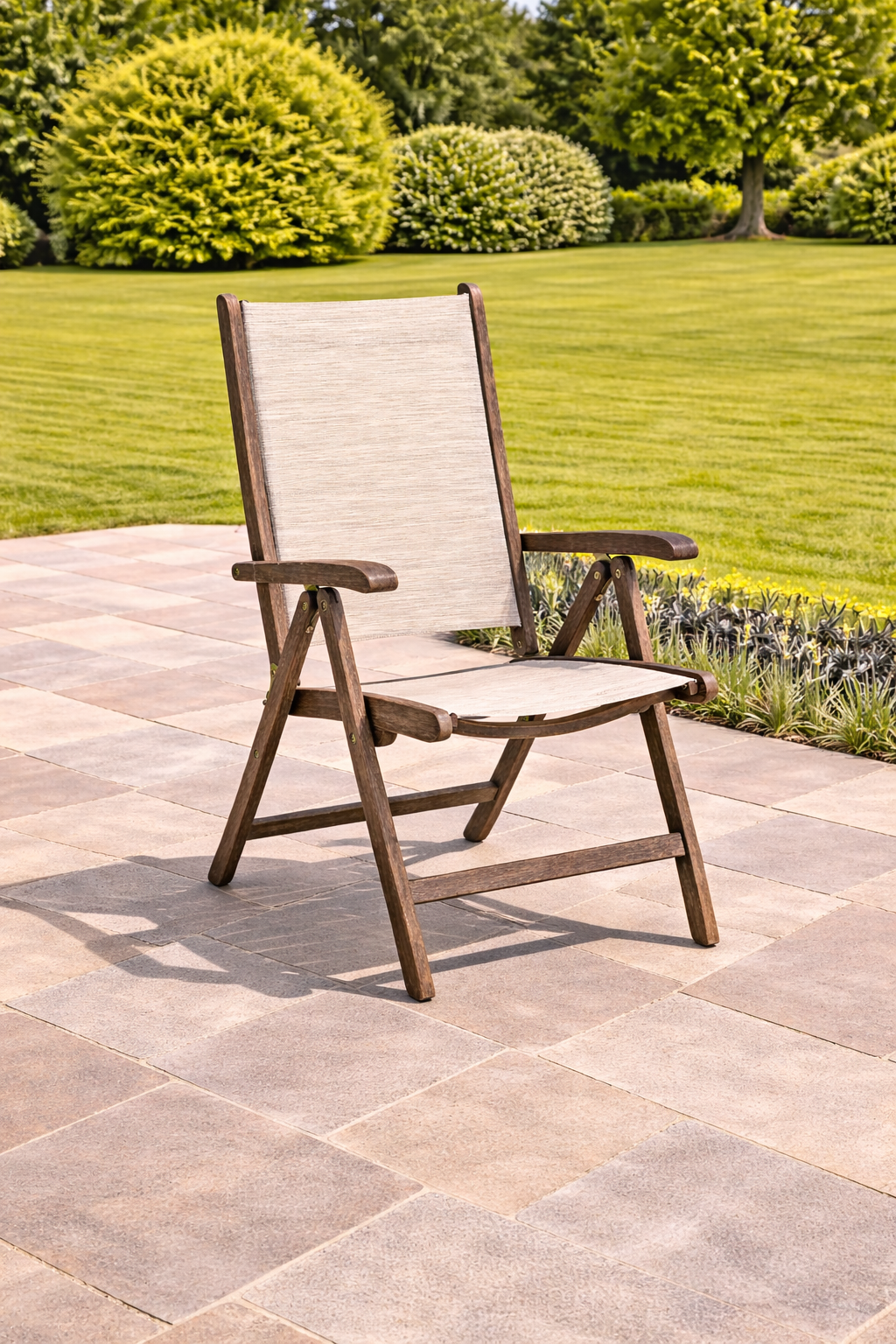 Beige and brown outdoor chair on a stone patio with green grass and bushes in the background