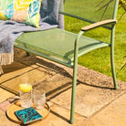 Green outdoor chair with a tray holding a drink and a book on a patio