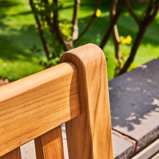 Close-up of a wooden chair with a blurred green garden background