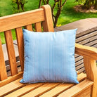 Blue pillow on a wooden bench with a green outdoor background