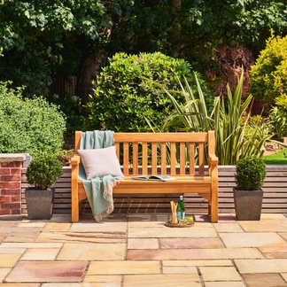 Wooden bench with a blanket and pillow on a patio surrounded by greenery