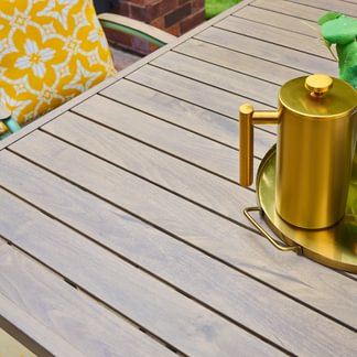 Gold teapot on a wooden table with a green chair and yellow cushion in the background