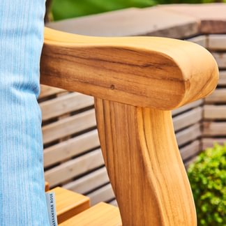 Wooden chair arm with a blurred background of greenery and wooden planks