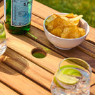 Bowl of crisps with a bottle and glasses on a wooden table surface