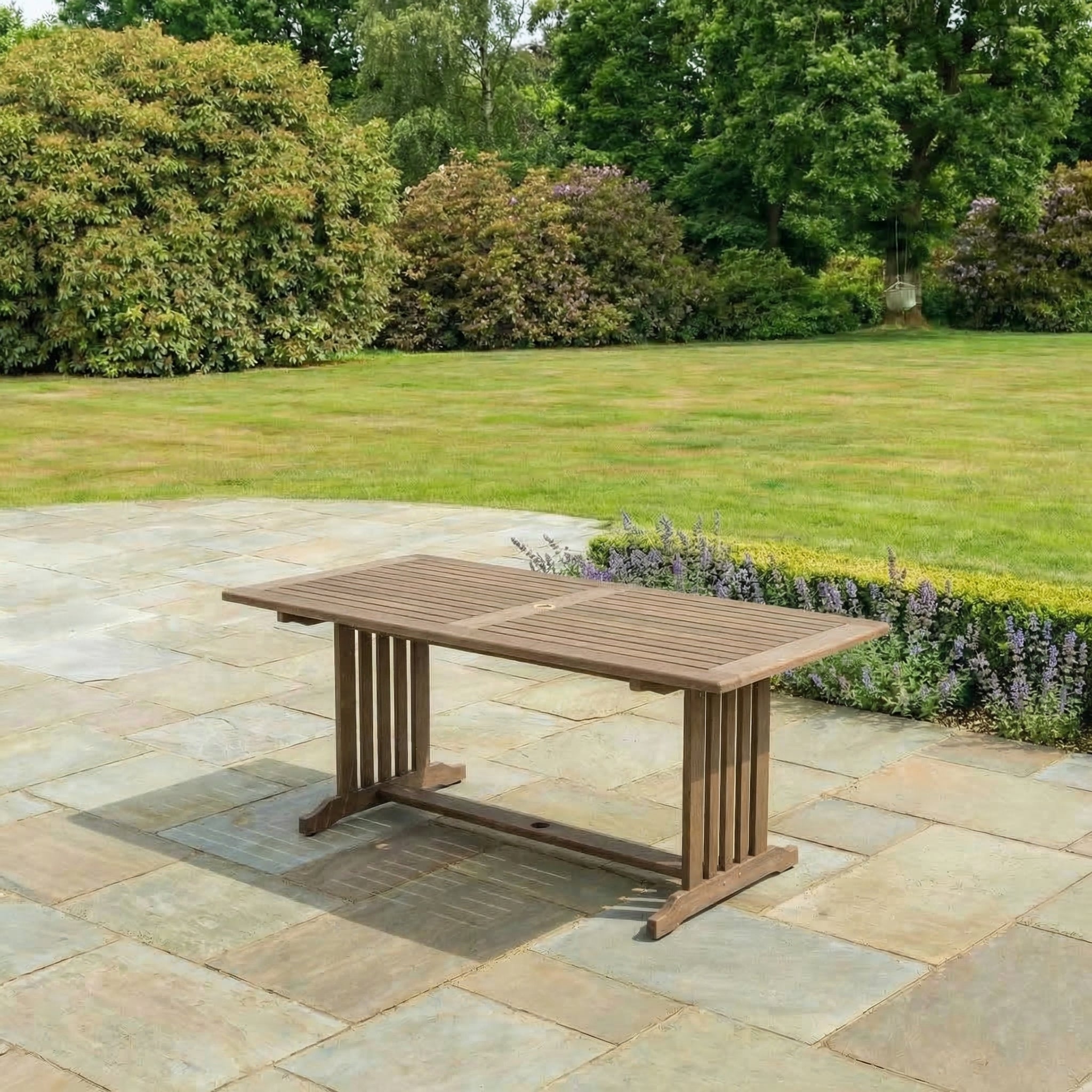 Wooden garden table on a stone patio with greenery in the background