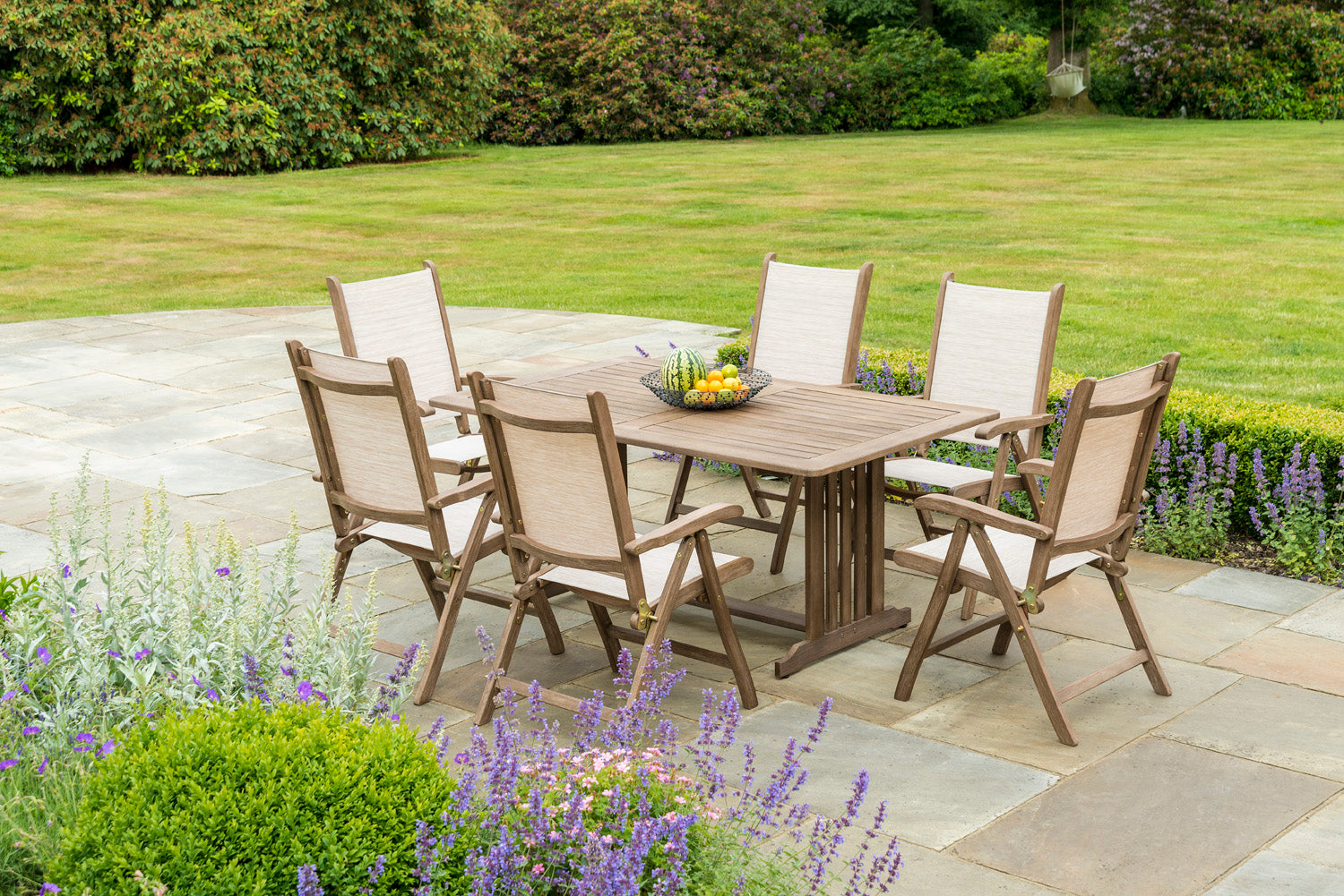 Sherwood wooden outdoor dining set for 6 on a stone patio with greenery scene in the background