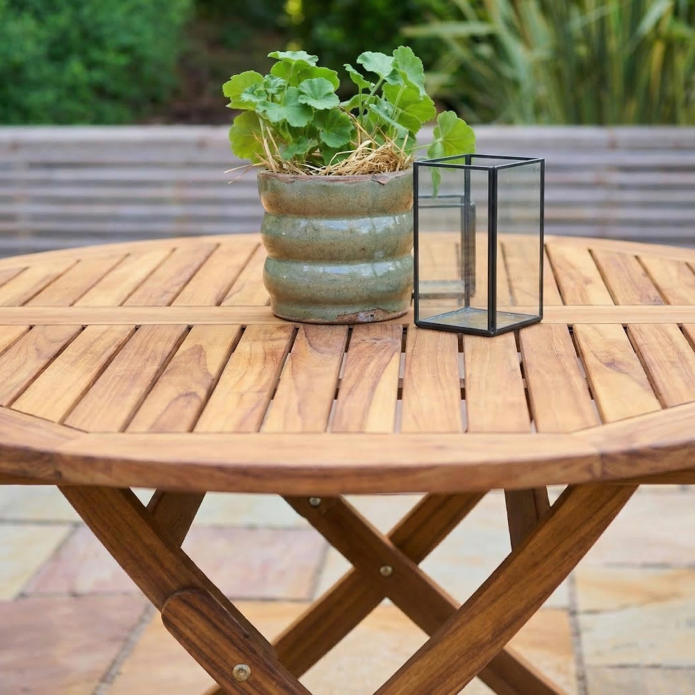 Wooden table with a potted plant and a black lantern on a blurred outdoor background