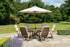 Outdoor patio set with table and 6 reclining chairs under a large parasol in a garden setting.