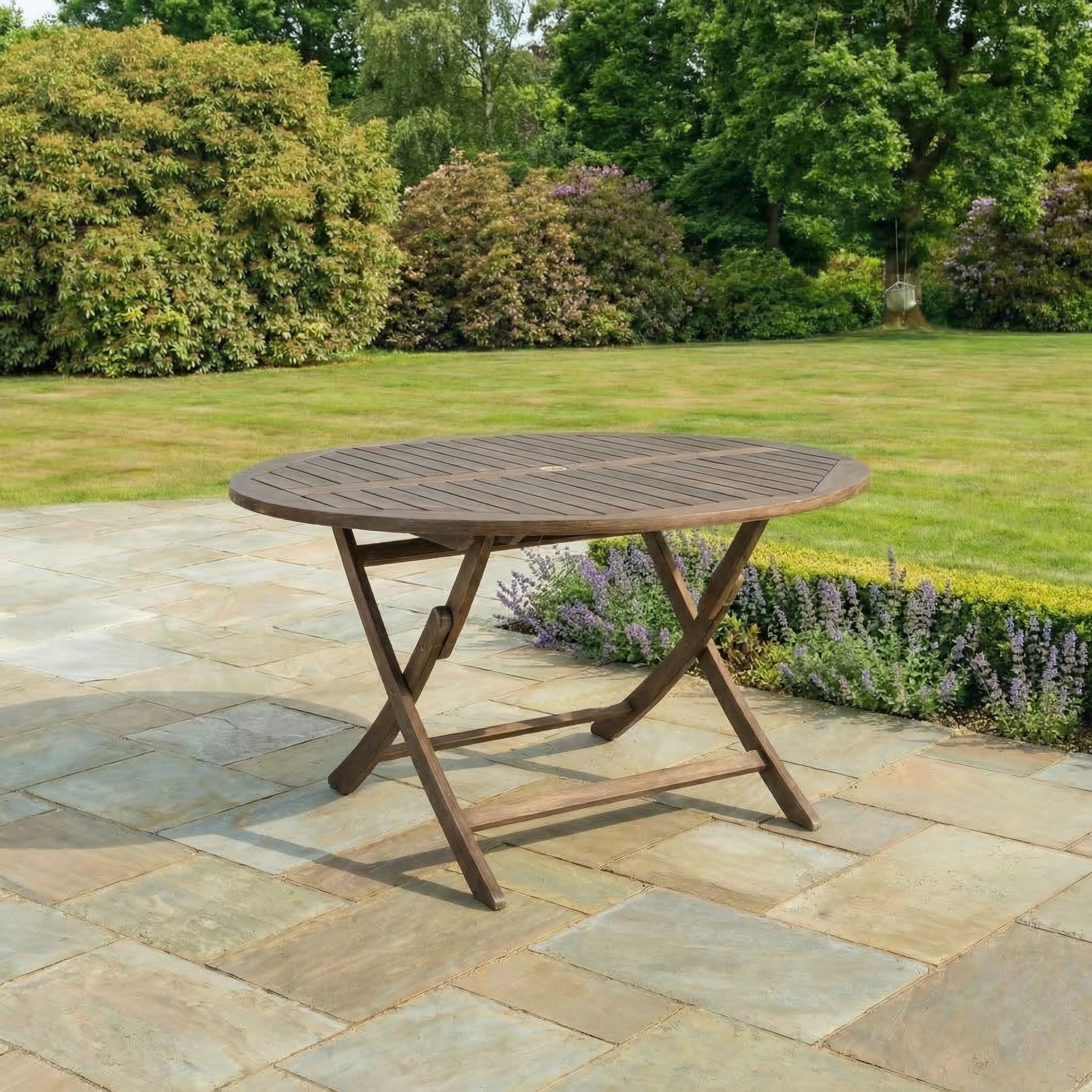 Wooden outdoor table on a stone patio with greenery in the background
