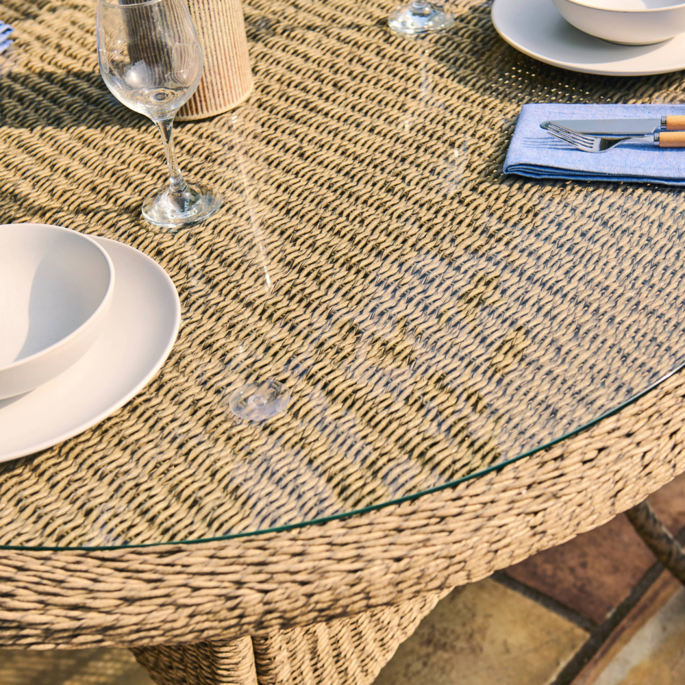 Round woven table with glass top, white plates, and a wine glass on a stone surface.