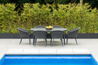 Outdoor dining set for six by a pool with a hedge in the background