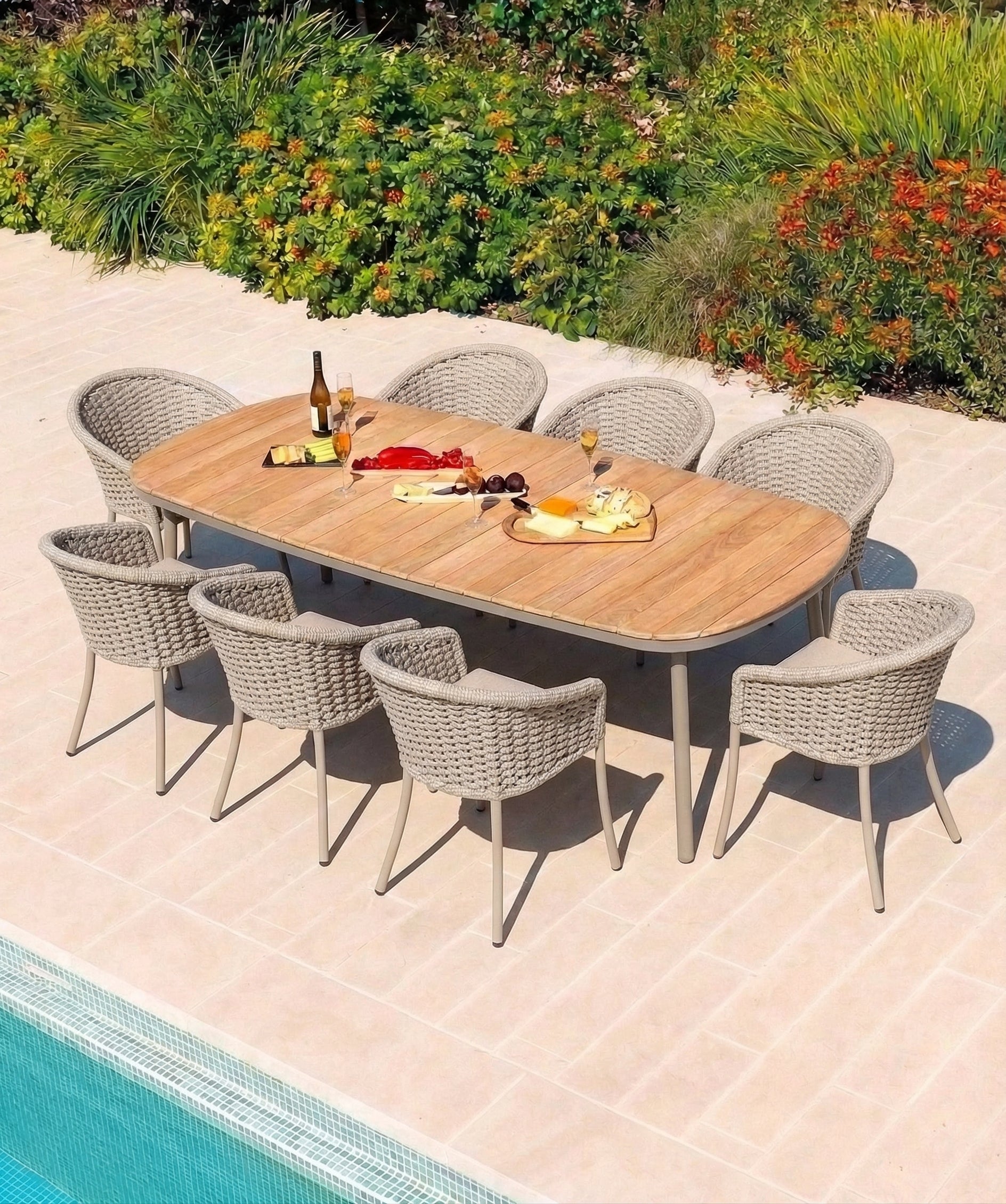 Outdoor dining setup with a wooden table and woven rope chairs by a pool