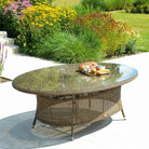 Outdoor luxury rattan oval table with glass top in a garden setting