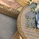 Round woven table with a glass top with a plate and plant on the table
