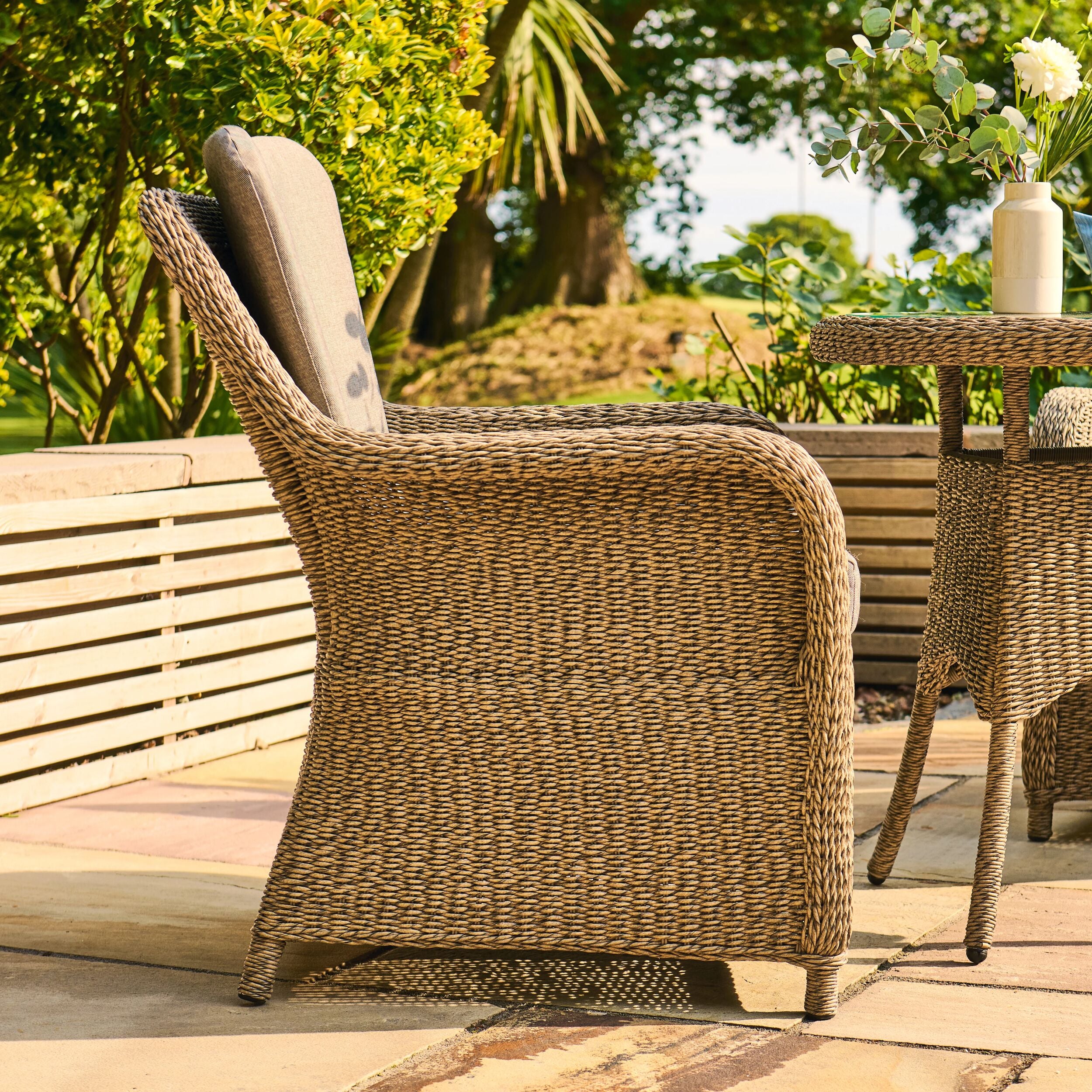 Wicker chair on a patio with a wooden table and flowers in the background
