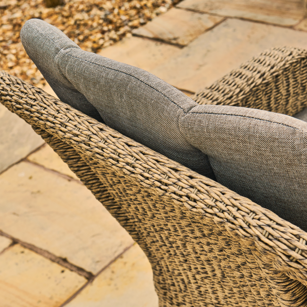Wicker chair with a grey cushion on a stone patio