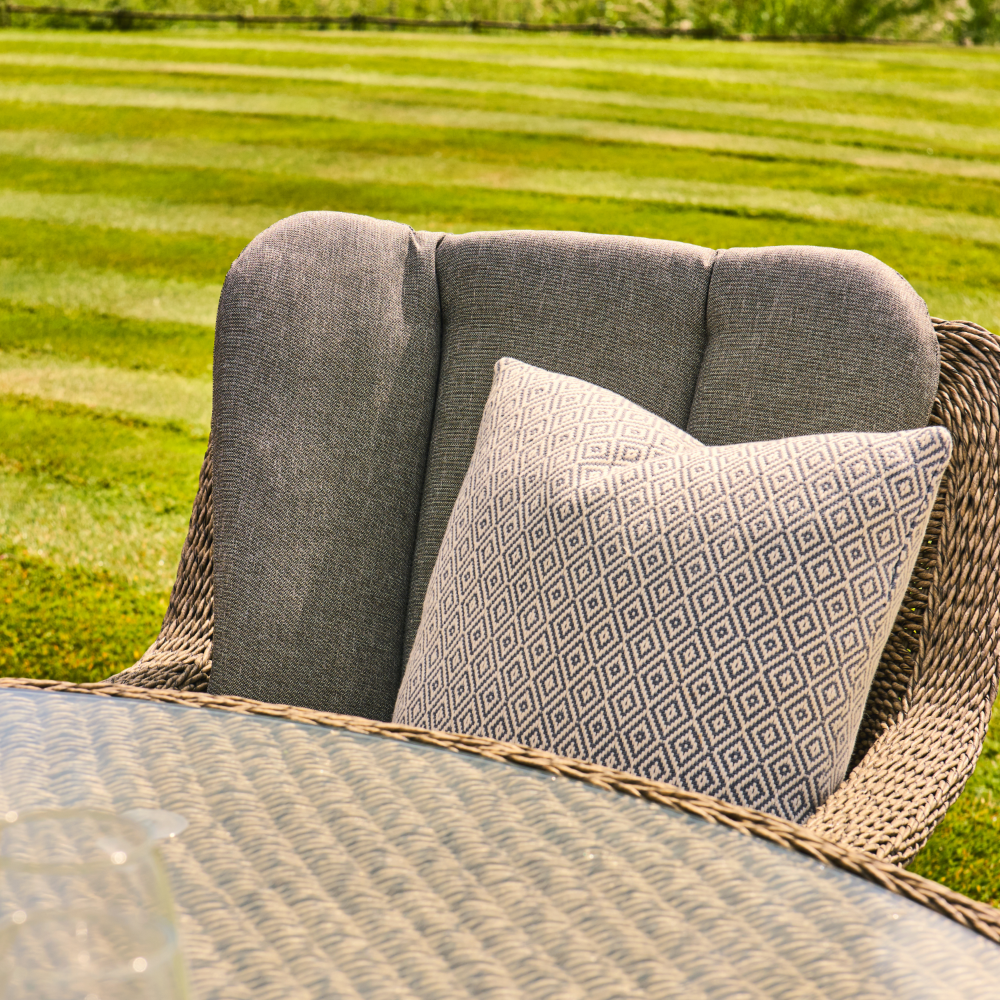 Grey cushioned chair with a patterned pillow on a grassy field