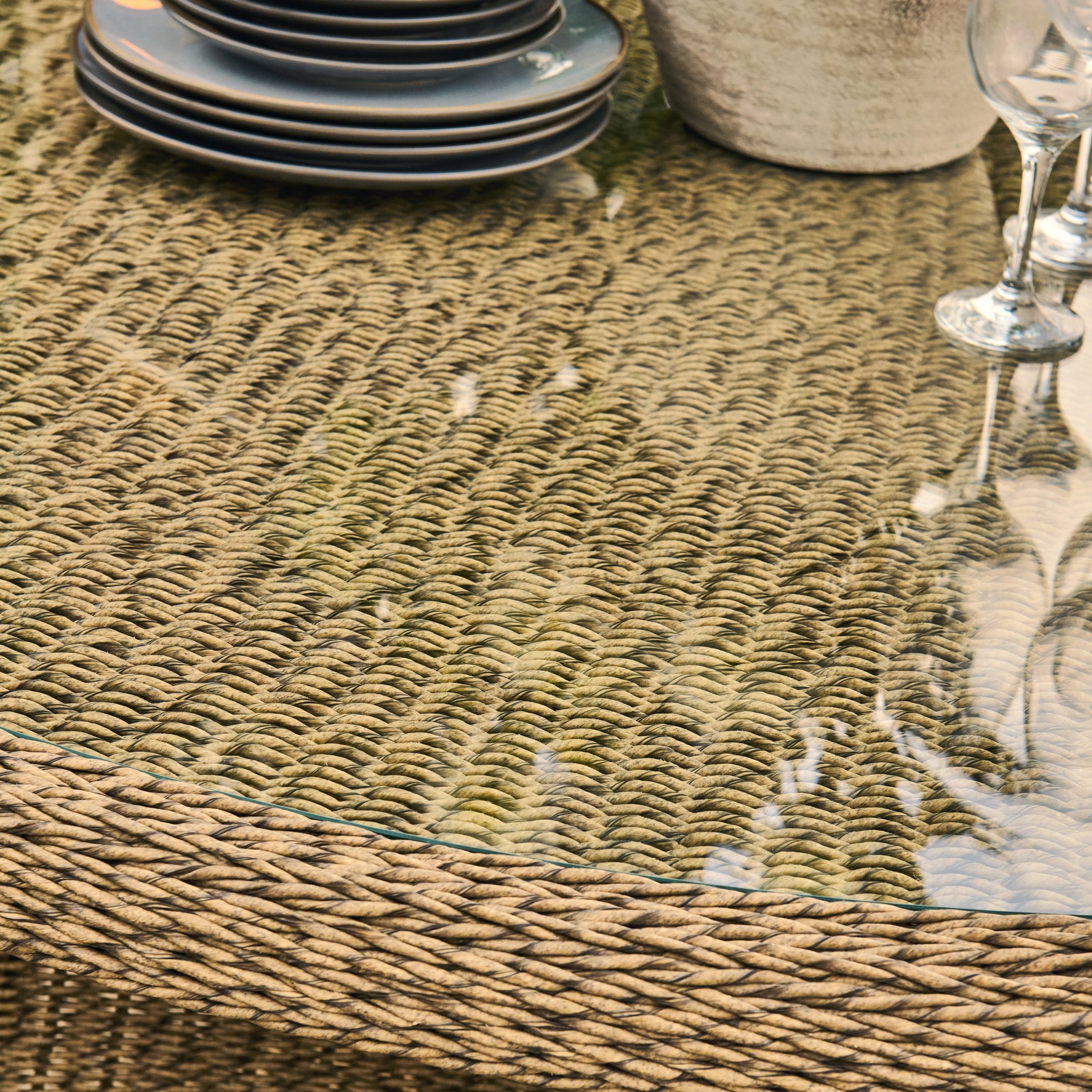 Wicker table with glass top and decorative items including plates and glasses.