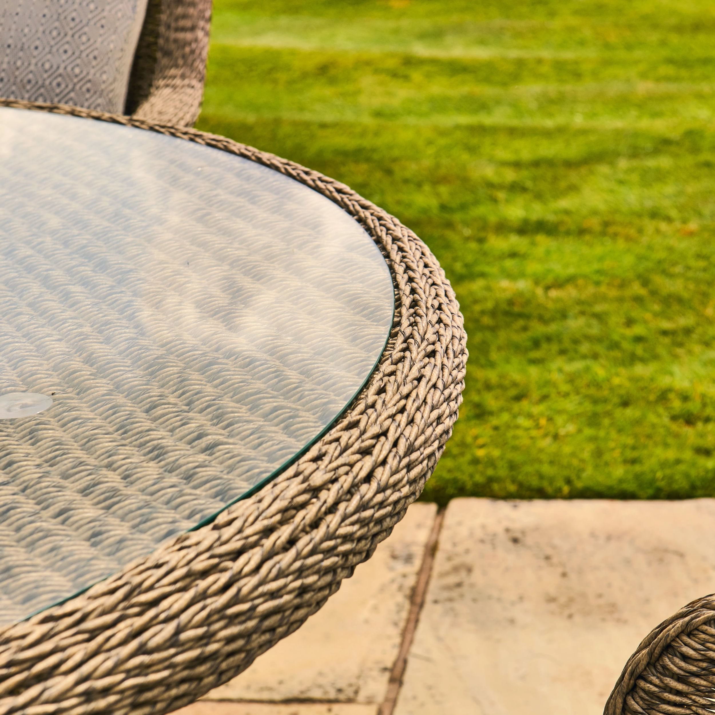 Glass-top table with woven edge on a patio with grass in the background