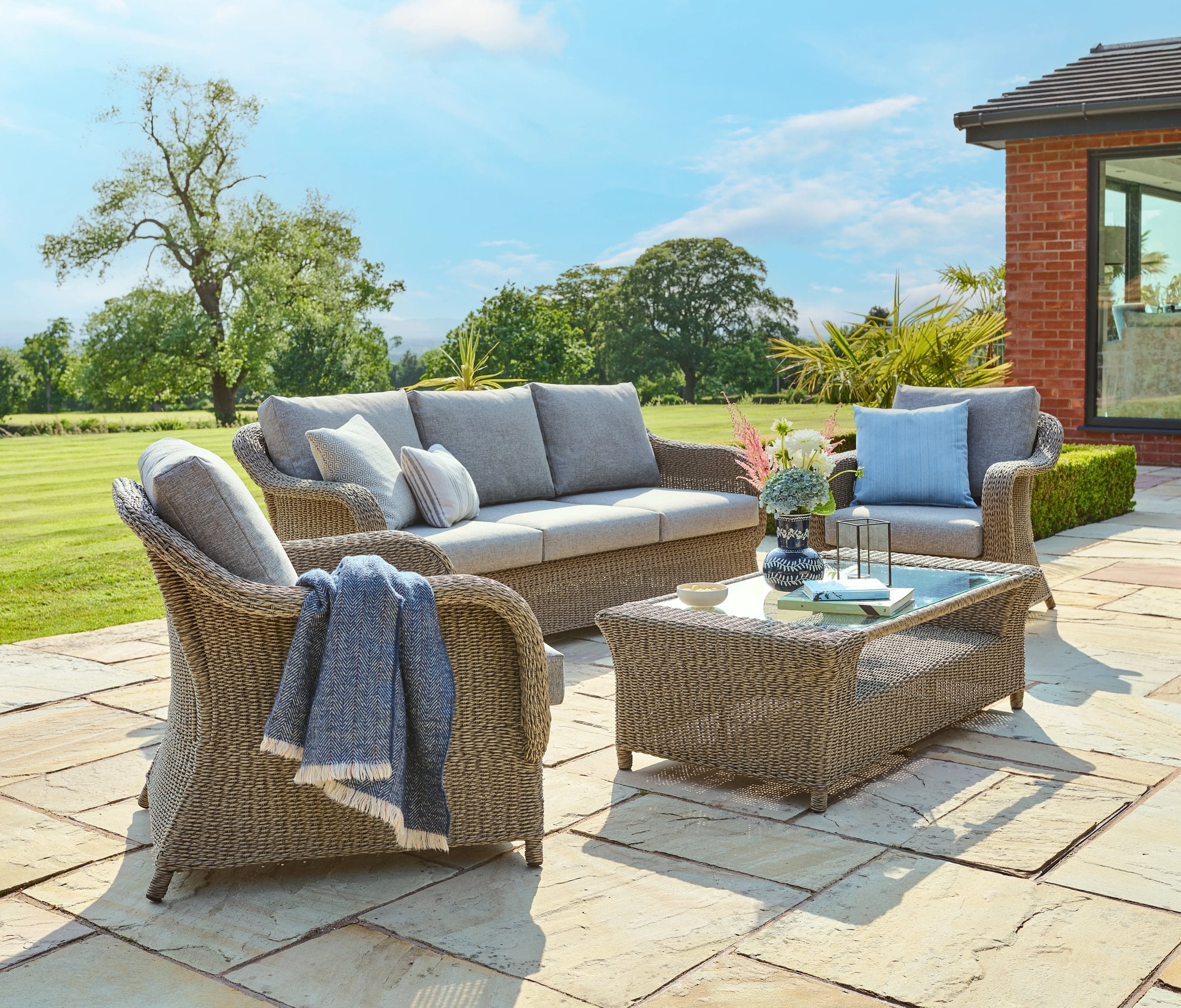 Outdoor patio set with wicker furniture and cushions on a stone patio.