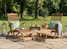 Two wooden lounge chairs with cushions on a patio area with a small table and plants.