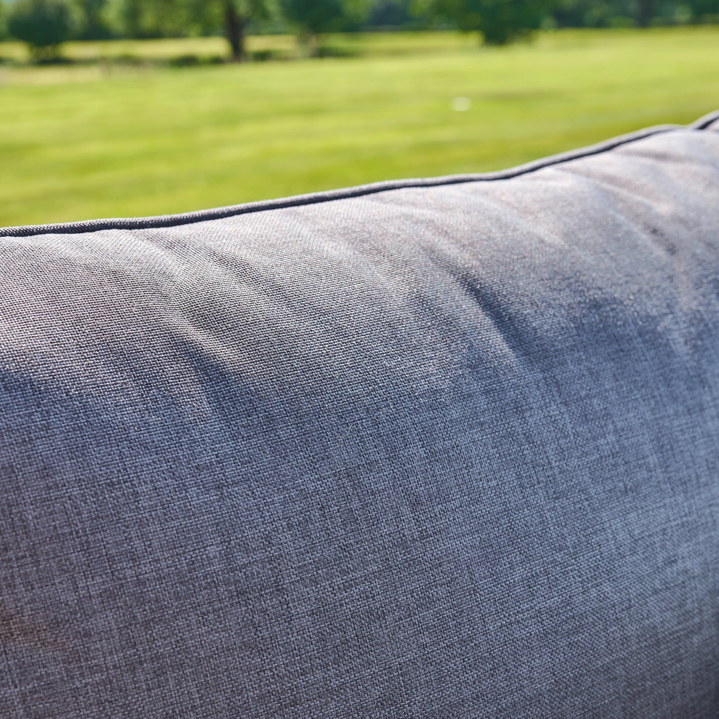 Close-up of a textured gray cushion with a blurred green field in the background