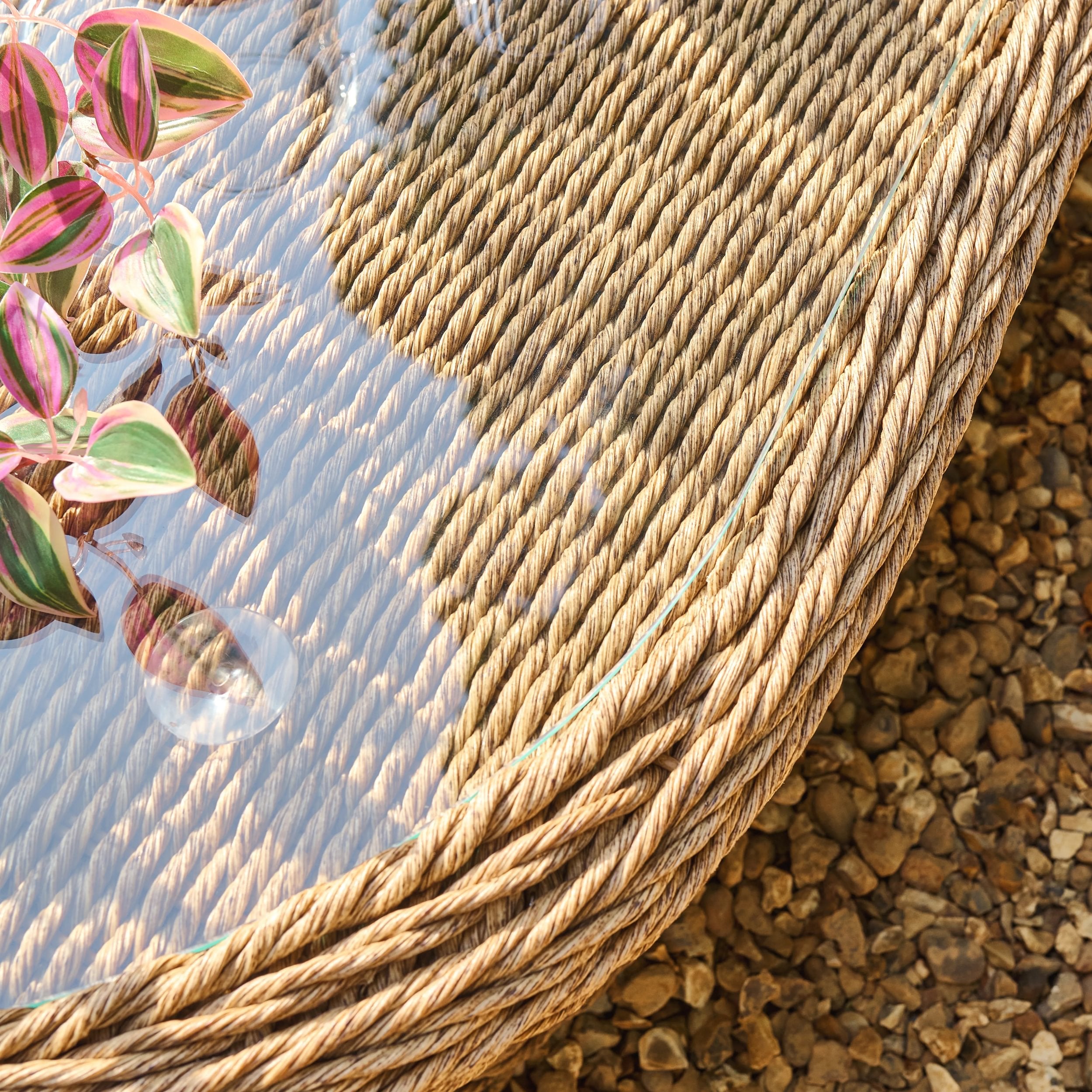 Close-up of a woven table with a plant and stones in the background