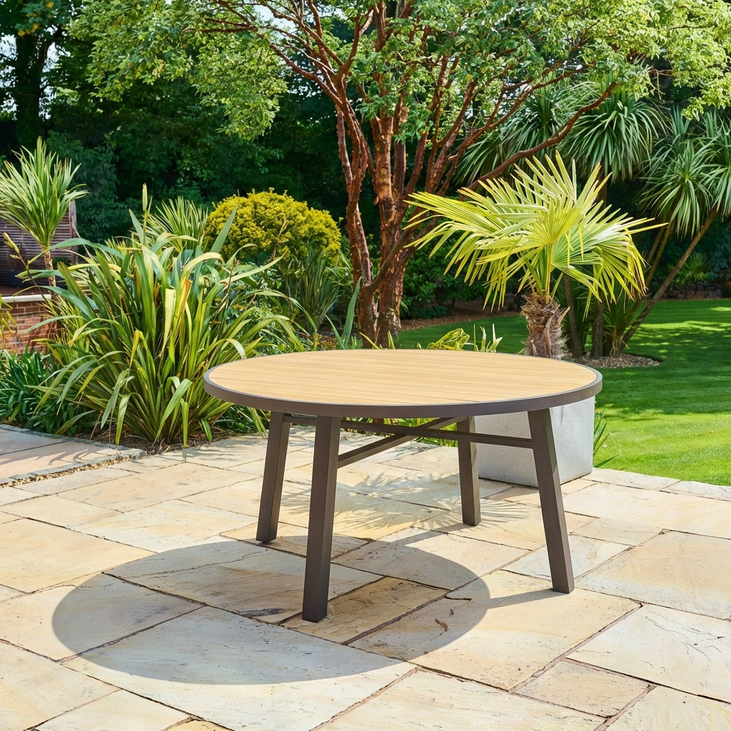 Round wooden outdoor table on a stone patio with greenery in the background