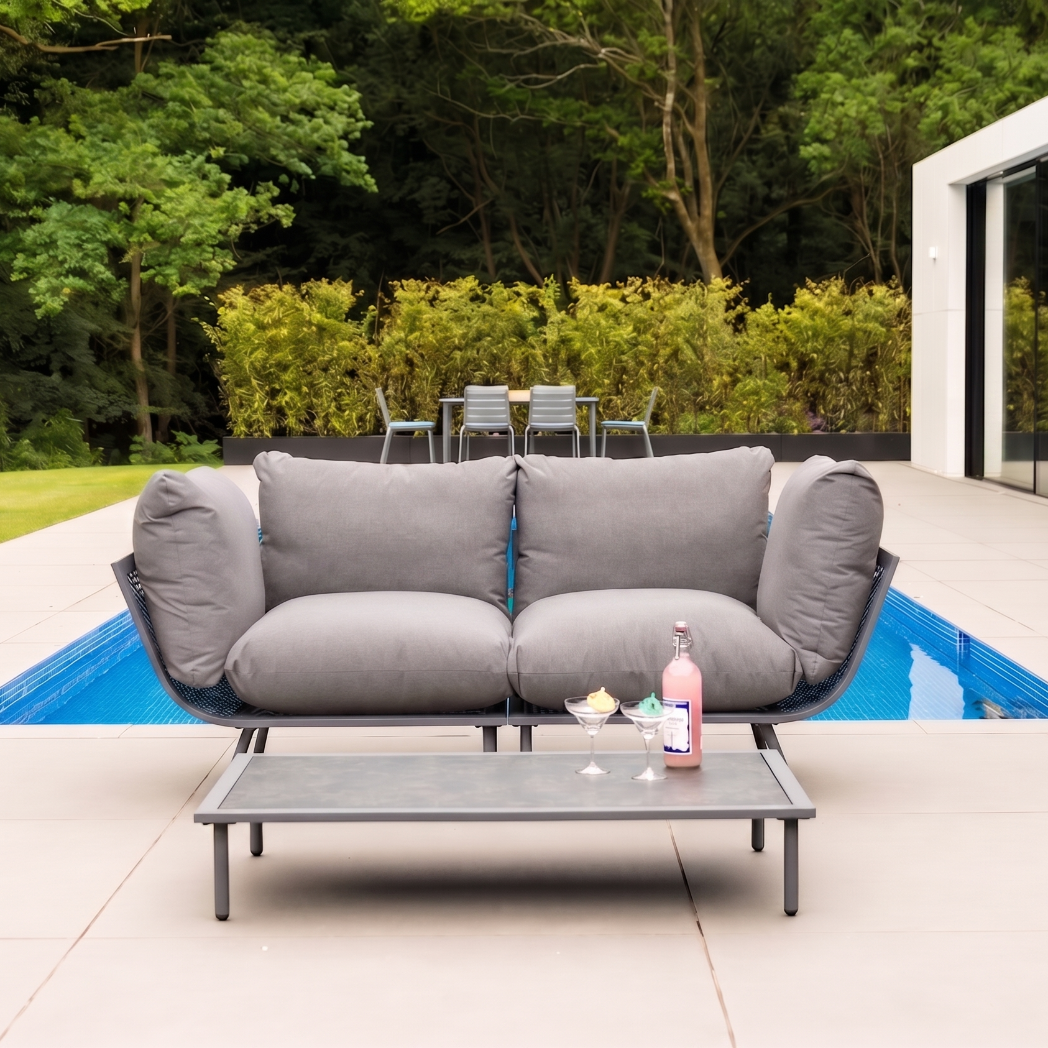 Gray outdoor sofa with a small table by a poolside, surrounded by greenery.