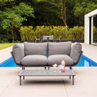 Gray outdoor sofa with a small table by a poolside, surrounded by greenery.