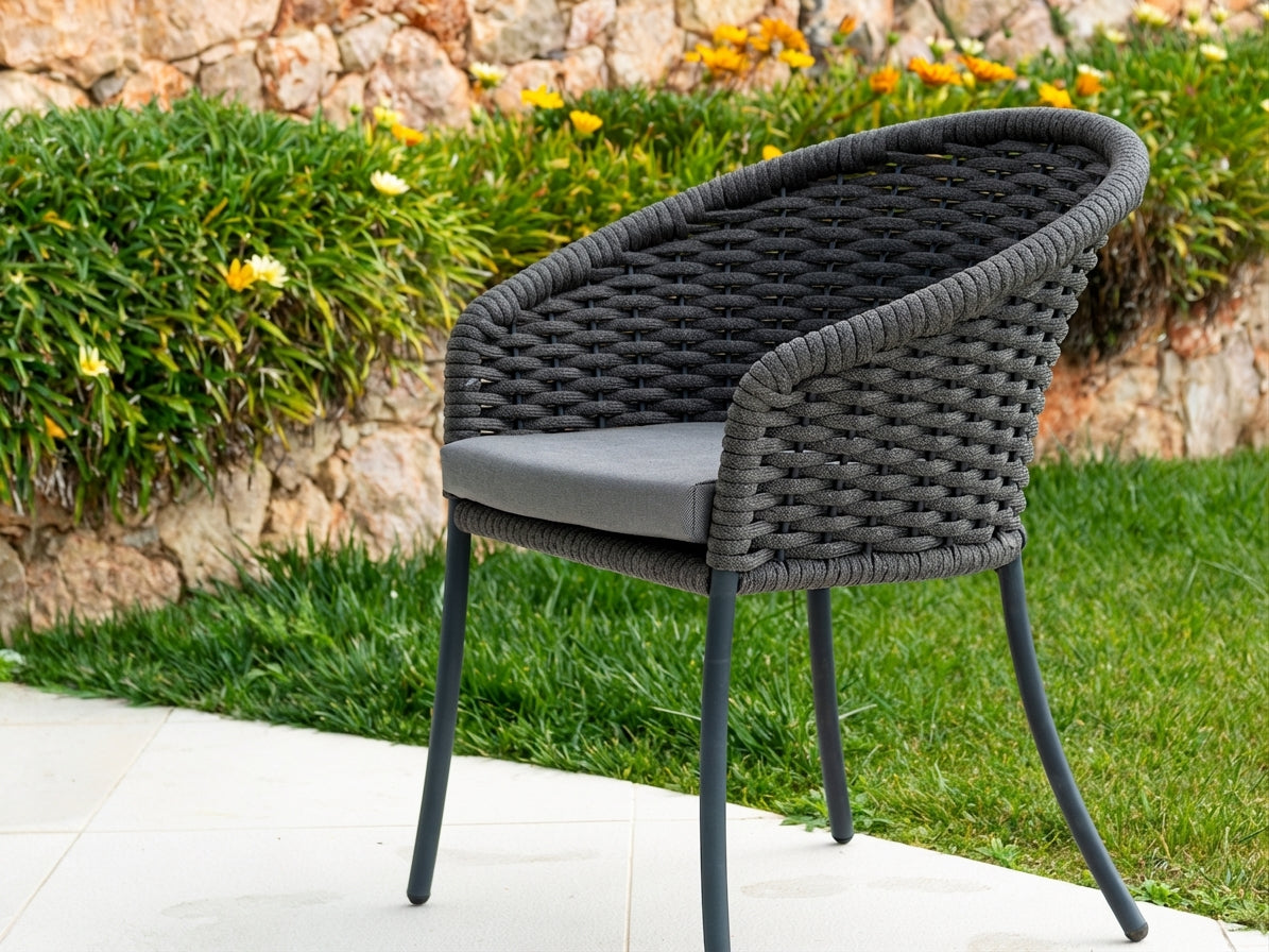 Rope weave chair with a cushion on a patio area with greenery and flowers in the background