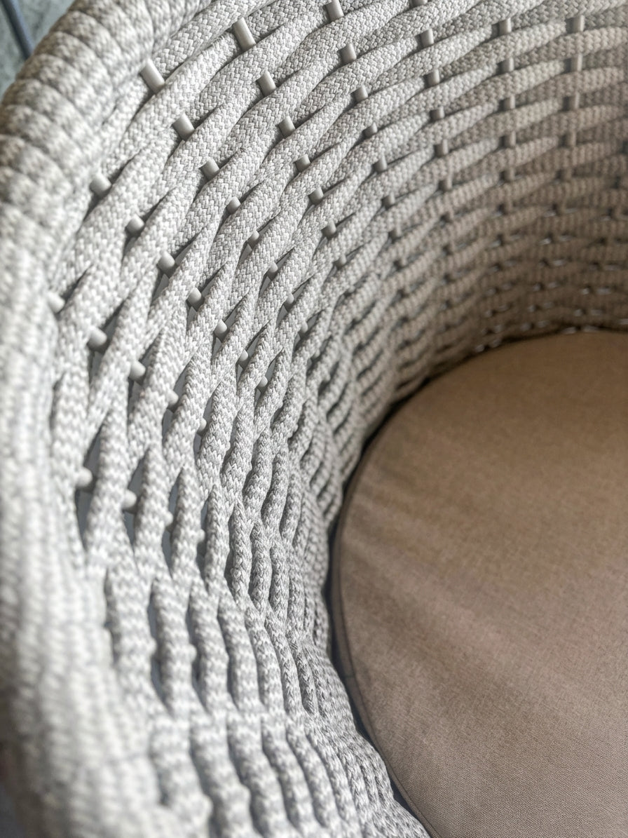 Close-up of a textured woven outdoor chair seat with a beige seat cushion.