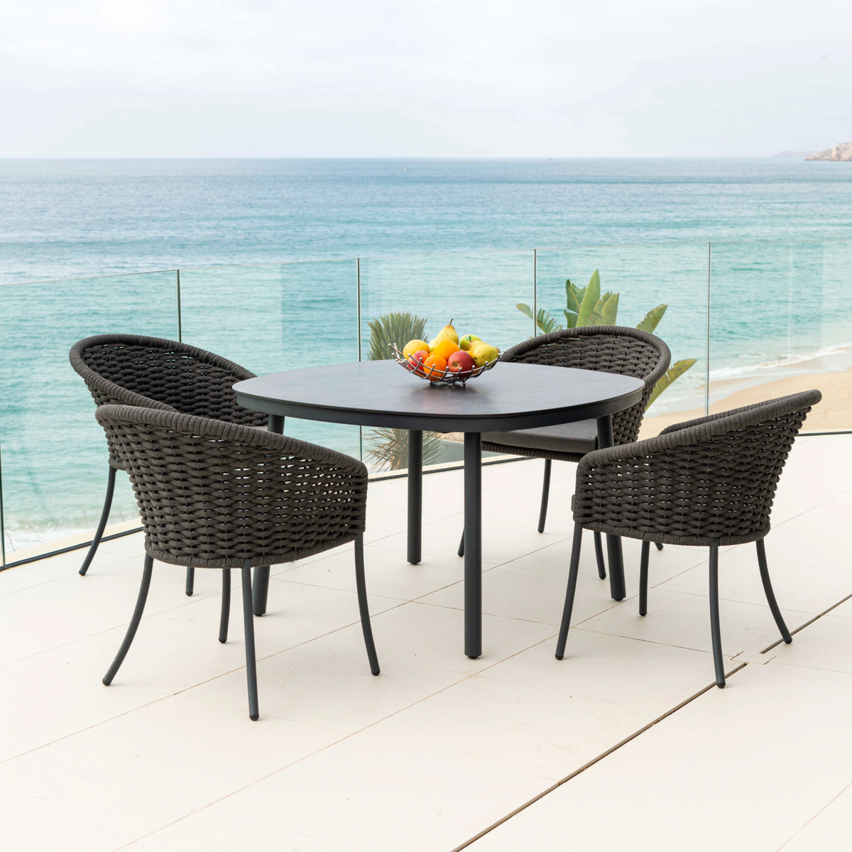 Outdoor Cordial dining set with round table and chairs on a balcony overlooking the ocean.