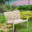 Wooden bench in a garden with plants and a tennis court in the background