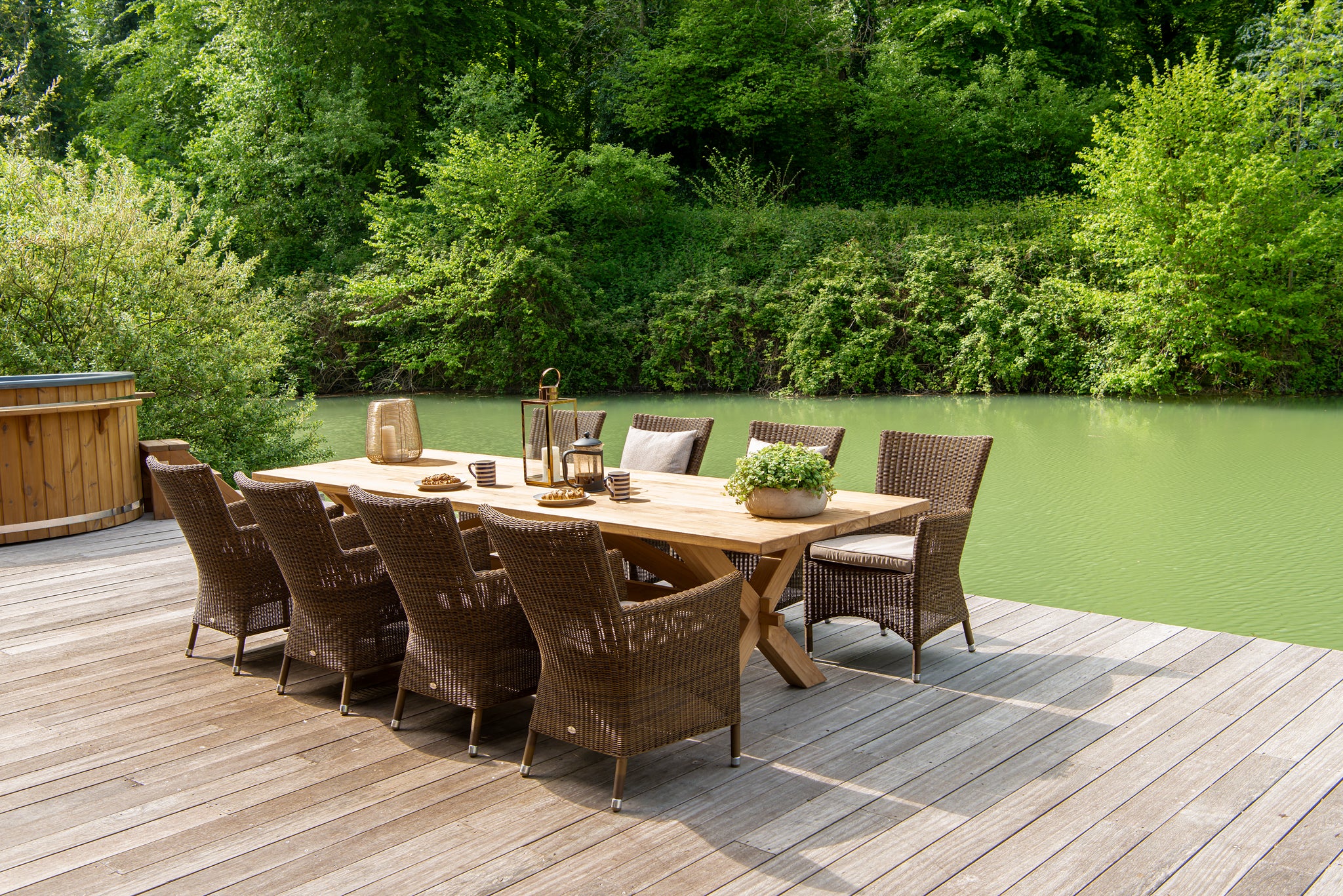 Teak rectangular dining table with luxury rattan armchair's besides a lake
