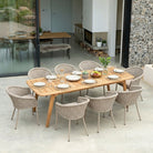 Wooden outdoor dining table with rope-woven chairs set up for a meal, in a modern outdoor living space.