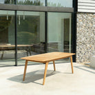 Wooden outdoor dining table in a modern patio setting with glass walls and stone wall.